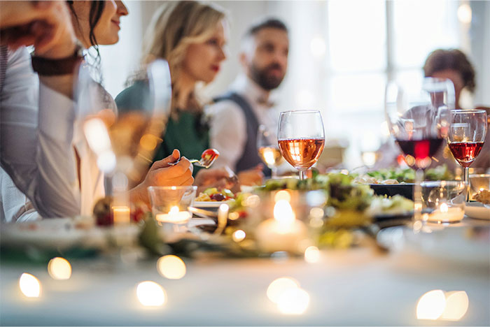Personas en una boda cenando con copas de vino y luces tenues, representando historias sobre bodas que fueron de mal en peor.