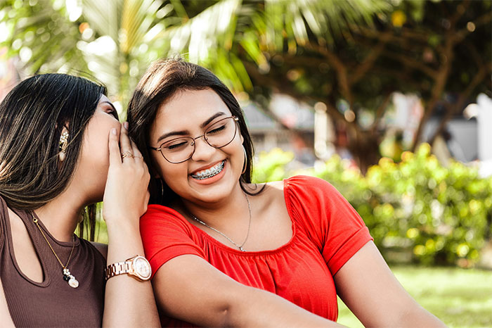Dos mujeres jóvenes compartiendo secretos y risas al aire libre, representando historias sobre bodas que fueron de mal en peor.