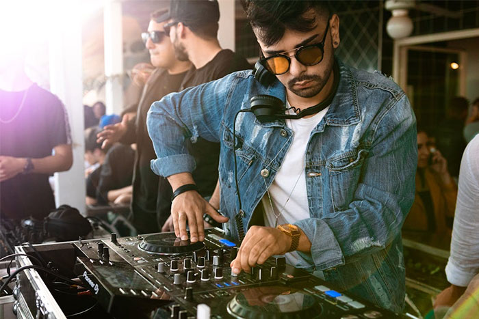 DJ con gafas y chaqueta de mezclilla mezclando música en boda, ilustrando historias de bodas que fueron de mal en peor.