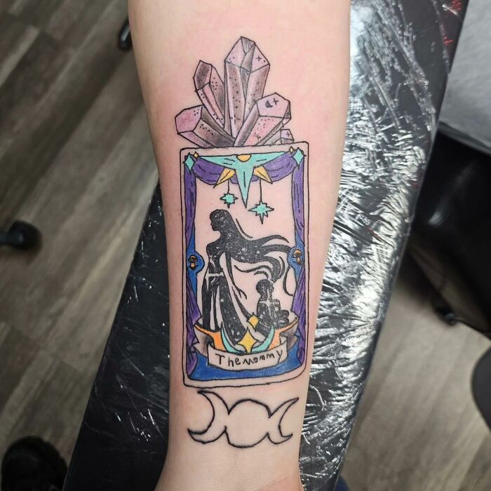 Tatuaje en brazo con diseño de cristal y figura oscura dentro de marco decorativo, ejemplo de tatuajes horribles difíciles de borrar.