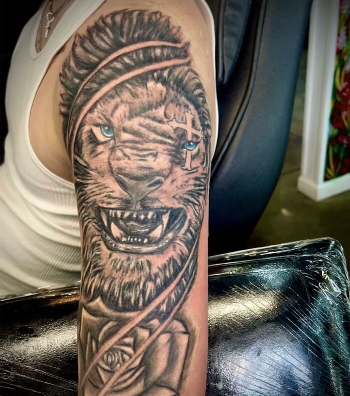 Tatuaje de león con ojos azules y cruz en la frente, ejemplo de tatuajes horribles difíciles de borrar.