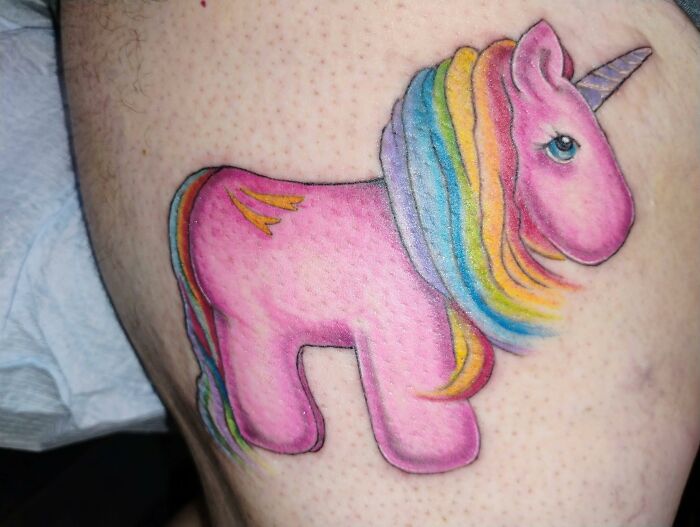 Tatuaje horrible de unicornio rosa con melena arcoíris en pierna, ejemplo de errores difíciles de borrar en tatuajes.