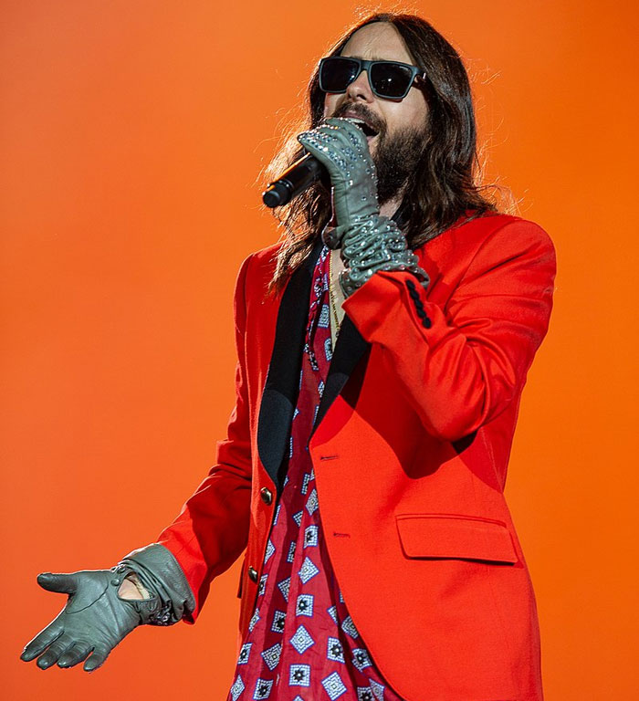Cantante con gafas de sol y guantes actuando en concierto, representando celebridades que hicieron algo horrible olvidado.