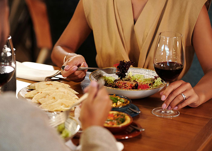 Pareja cenando en restaurante, disfrutando comida y vino, escena común en citas terribles según camareros que las presenciaron.