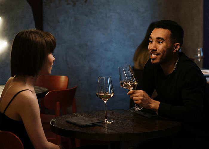Pareja en una cita en un restaurante, conversando y brindando con copas de vino blanco, escena de citas terribles.