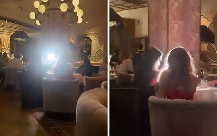 Influencers vergonzosos grabando video con luces brillantes en un restaurante elegante lleno de gente sentada.