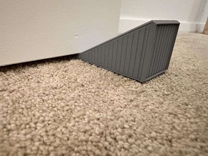 Tope de puerta gris sujetando puerta en piso alfombrado, consejos útiles y poco comunes para mujeres que viven solas.