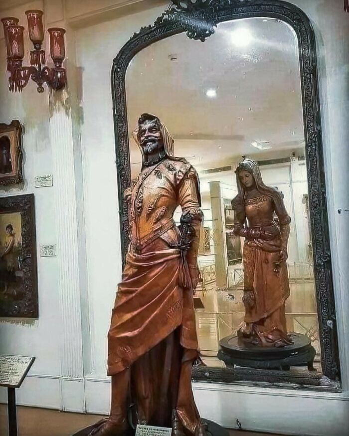 Estatuas arqueológicas reflejadas en espejo antiguo dentro de museo, destacando descubrimientos arqueológicos históricos.