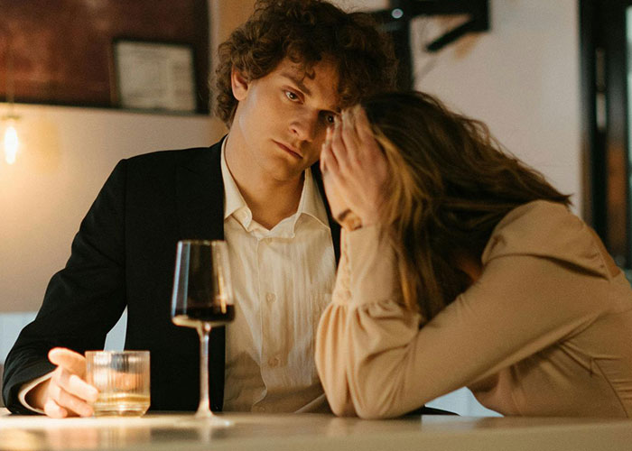 Pareja en una cita terrible en restaurante con camarero observando, reflejando momentos incómodos y tensos entre ellos.