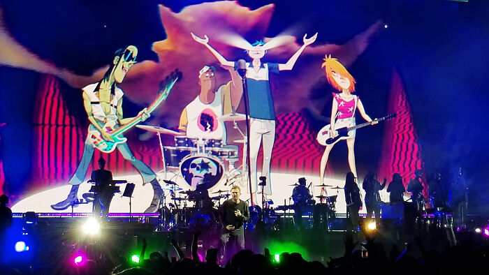 Concierto con pantalla animada mostrando banda, ilustrando momentos de confusión y correcciones fallidas en público.