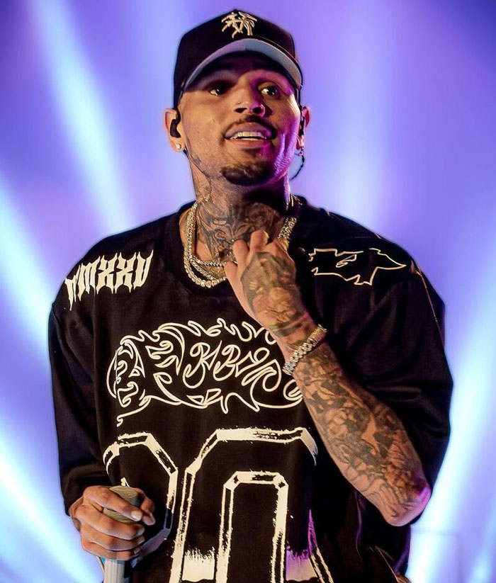 Cantante con tatuajes en brazo y cuello, gorra negra, durante presentación en vivo sobre escenario con luces. Celebridades horribles.