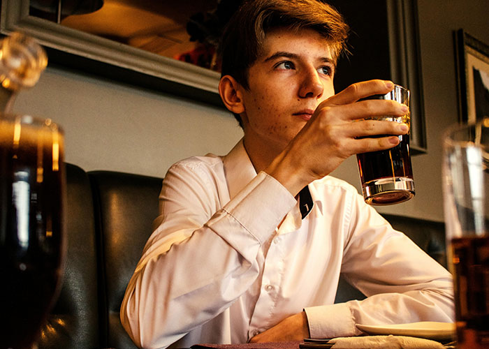 Joven camarero en restaurante tomando una bebida oscura, representando citas terribles presenciadas en el servicio.