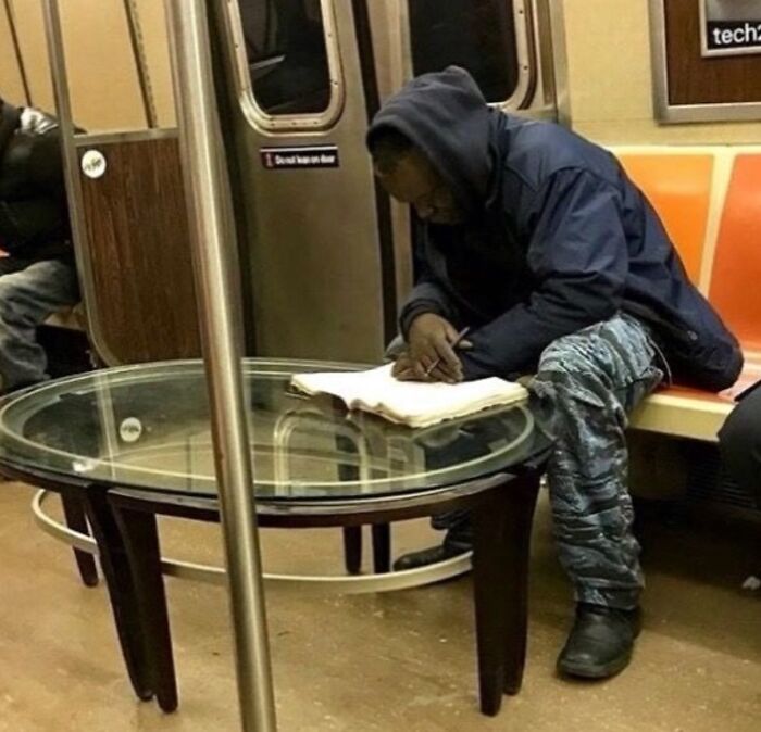 Hombre con sudadera y pantalones camuflaje escribiendo en un cuaderno sobre una mesa de cristal en el metro, imagen maldita.