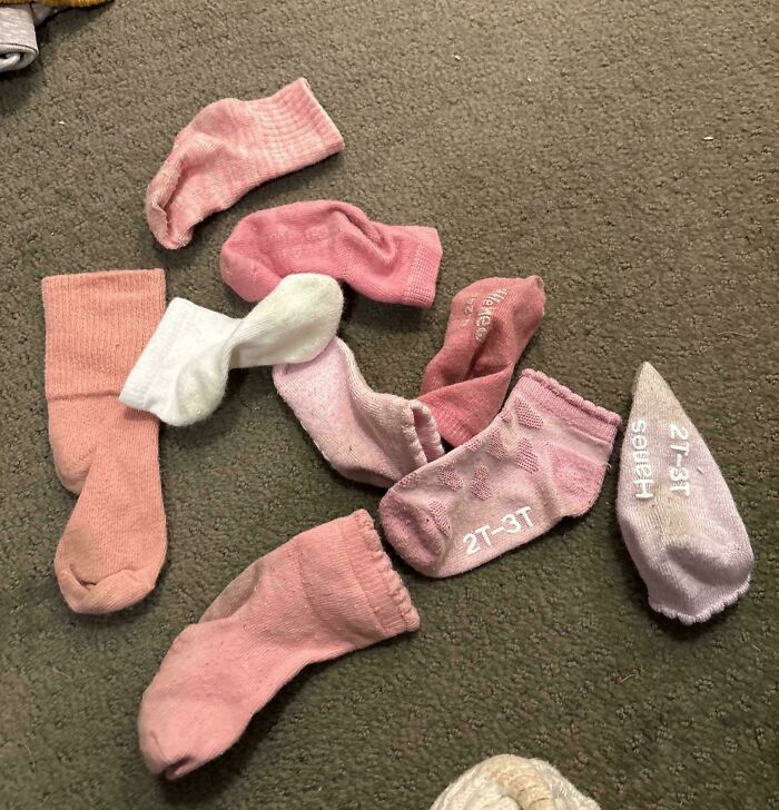 Calcetines de bebé desparejados y desorden en suelo, reflejando un día difícil para padres y madres.