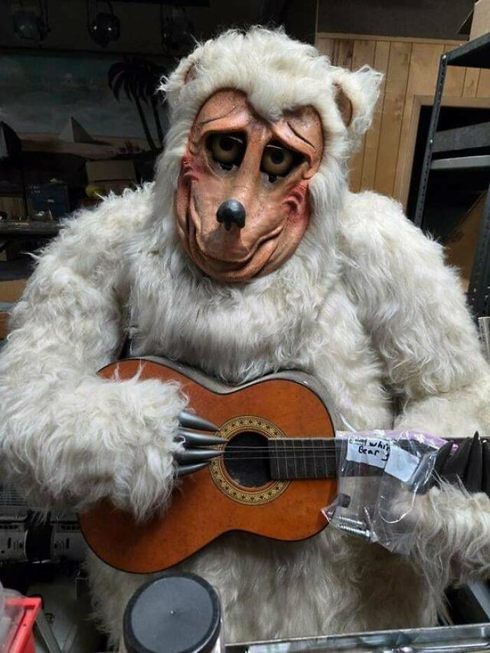Muñeco aterrador con disfraz de oso blanco tocando guitarra en ambiente inquietante y oscuro.