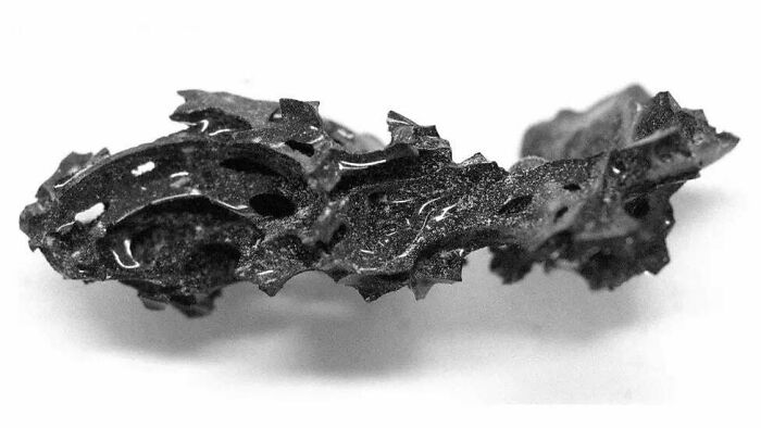 Fragmento oscuro y quemado con textura irregular y agujeros, imagen aterradora e inquietante en blanco y negro.