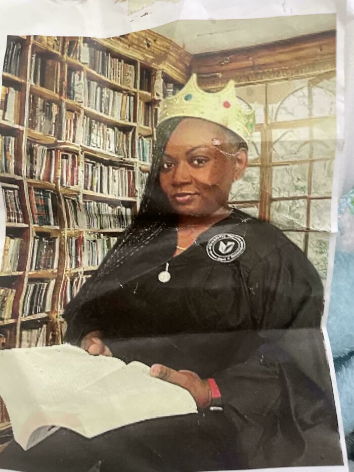 Mujer con toga y corona en biblioteca, imagen confusa y divertida que podría necesitar contexto para entenderse.