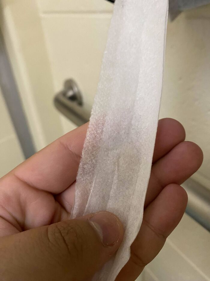 Mano sosteniendo papel higiénico sucio en un lugar de trabajo tóxico mostrando condiciones poco higiénicas.