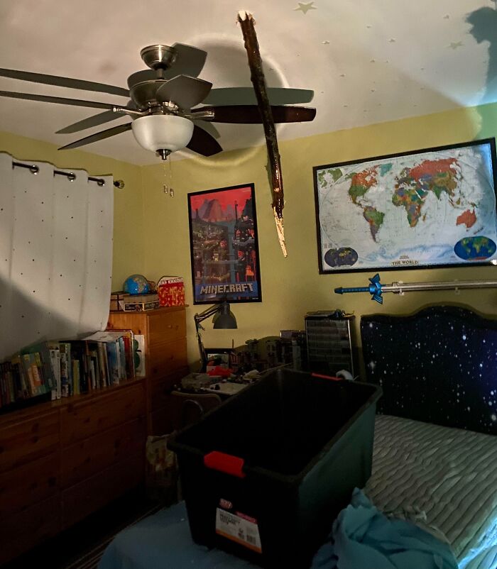 Habitación desordenada con padre usando cubeta para recoger pedazo de techo caído, reflejando día difícil para padres y madres.