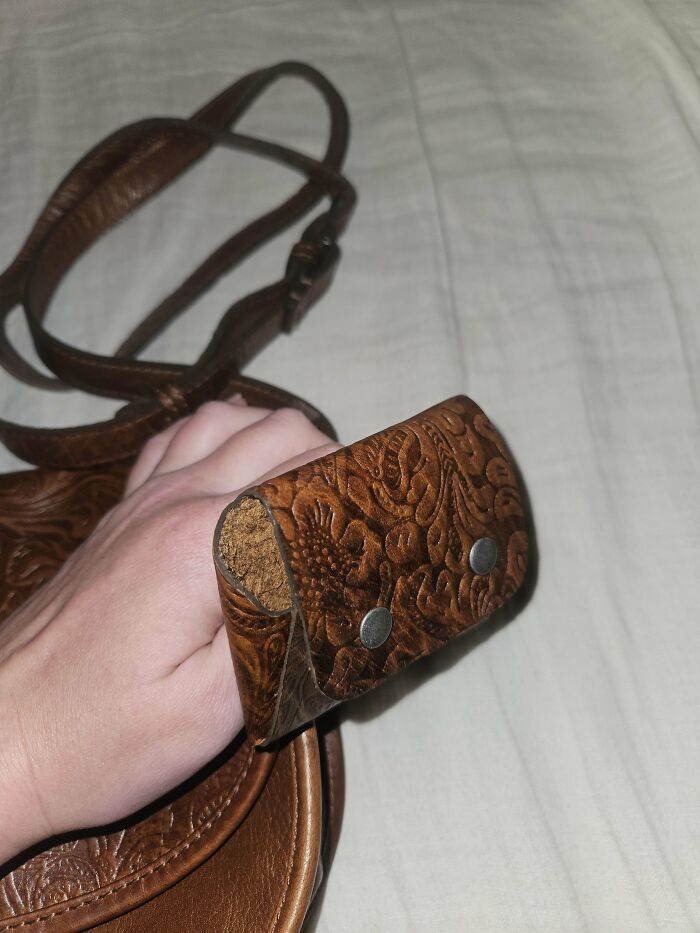 Bolso de cuero marrón con diseño grabado y correa, mostrando desgaste en la esquina frontal, personas sin idea piden ayuda.