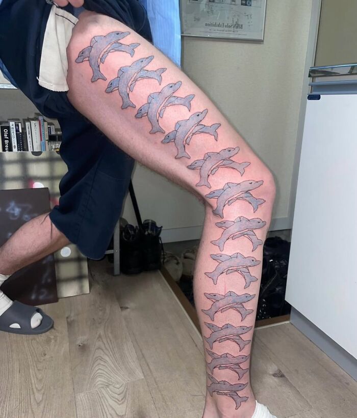 Tatuaje horrible de delfines repetidos en toda la pierna, un claro ejemplo de errores difíciles de borrar.