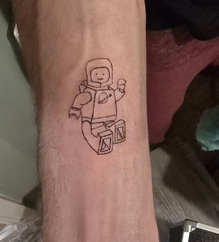 Tatuaje horrible de muñeco LEGO astronauta en brazo, ejemplo de errores difíciles de borrar en tatuajes.