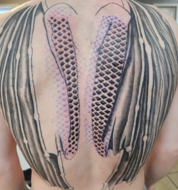 Tatuaje en la espalda con diseño de piel rasgada y escamas, ejemplo de tatuajes horribles difíciles de borrar.