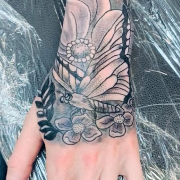 Tatuaje en mano con diseño de mariposa y flores en negro y gris, ejemplo de tatuajes horribles difíciles de borrar.