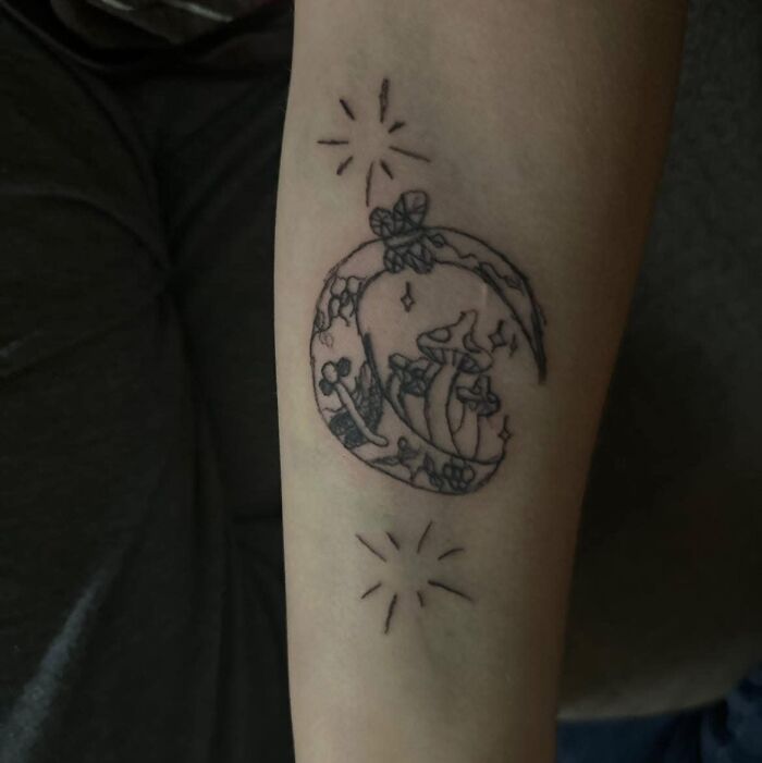 Tatuaje negro con diseño de luna y hongos en brazo, ejemplo de tatuajes horribles difíciles de borrar.