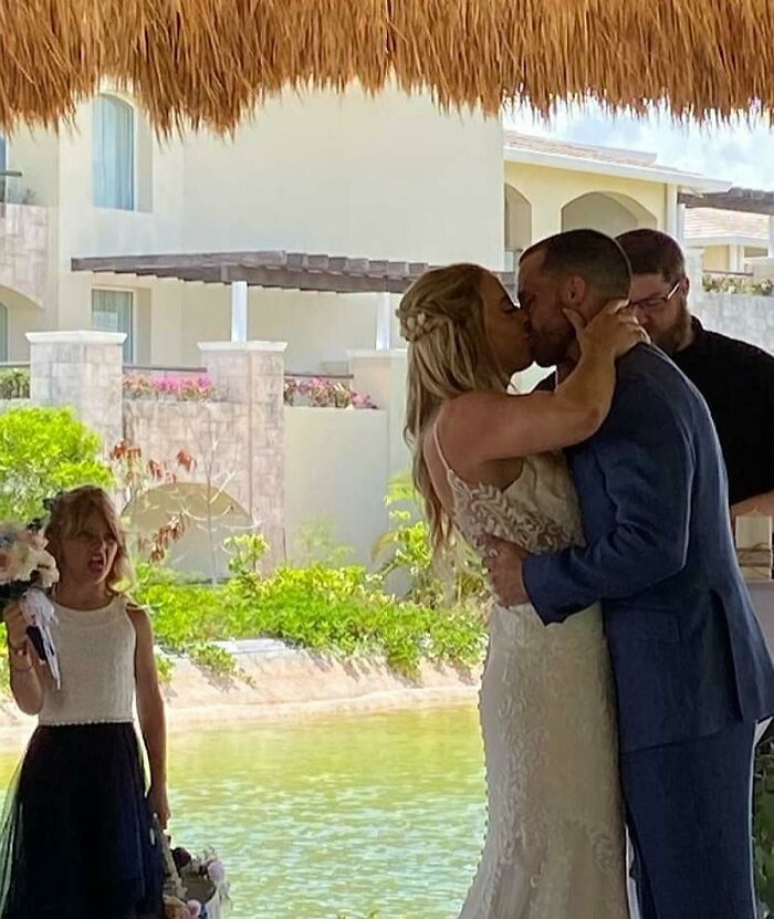 Niña haciendo una expresión divertida mientras una pareja se besa en una boda, fotos para hacerte reír hoy.