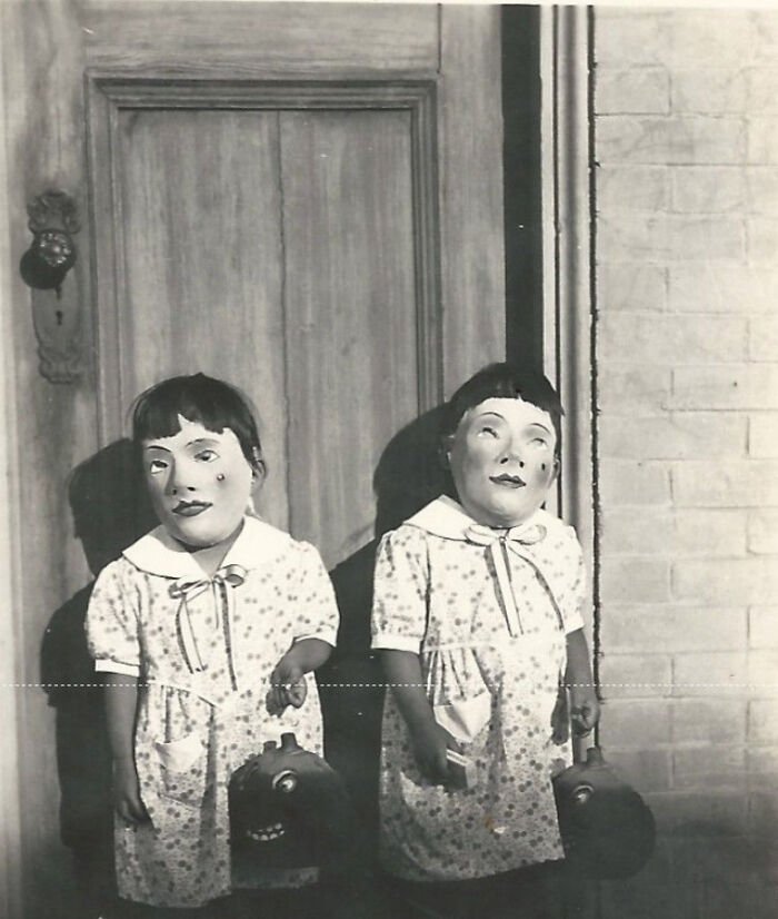 Niños con disfraces inquietantes y máscaras antiguas frente a una puerta en una foto impactante del pasado.
