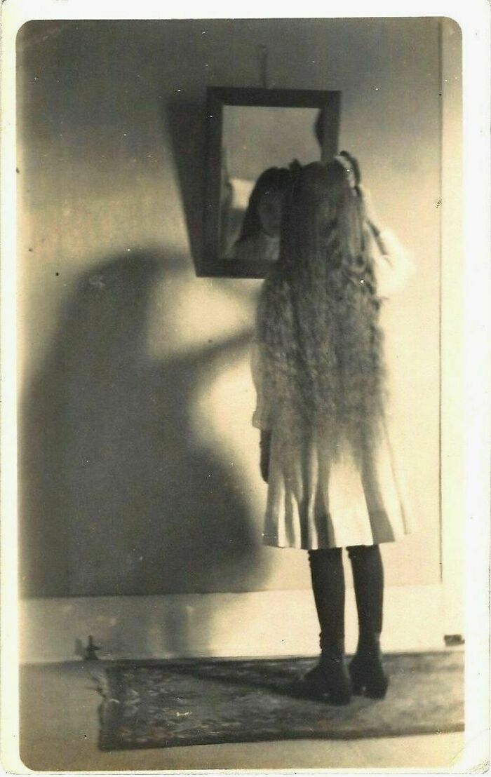 Niña de espaldas frente a espejo con largo cabello y sombra misteriosa en foto del pasado inquietante.