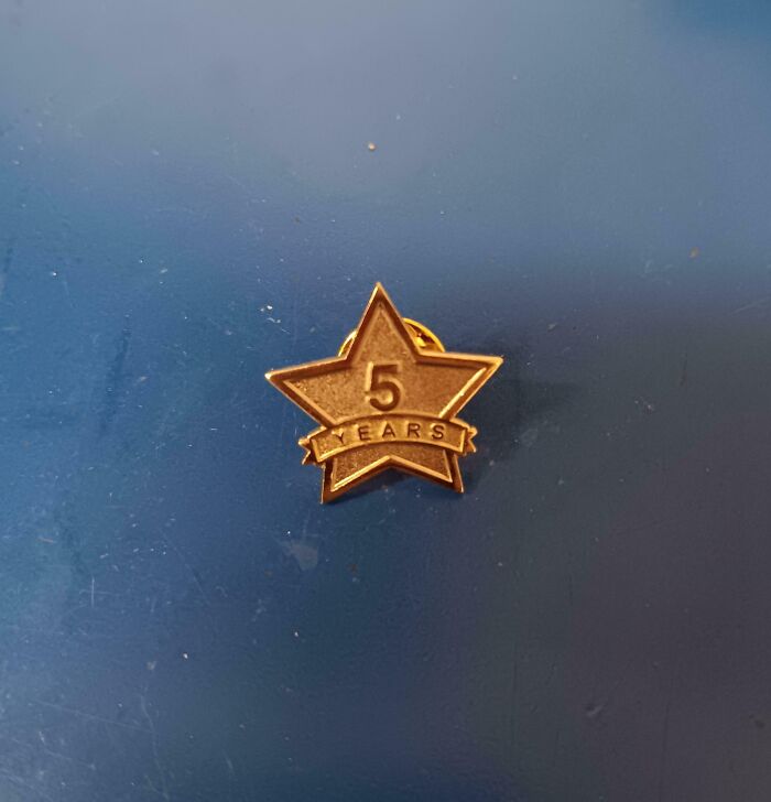 Pin dorado en forma de estrella con inscripción cinco años sobre superficie azul en entorno de lugares de trabajo tóxicos.