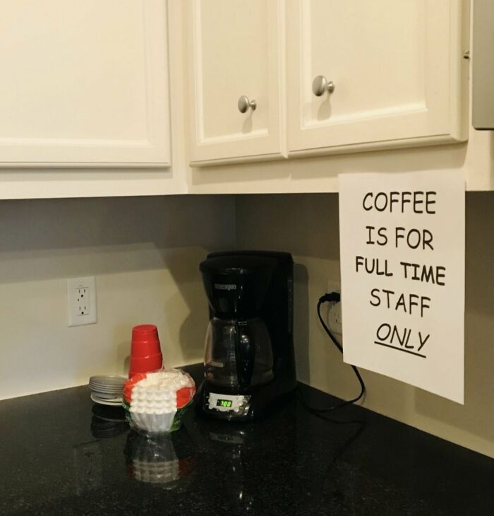 Cafetera en lugar de trabajo con cartel que limita el café solo al personal de tiempo completo, ambiente tóxico evidente.