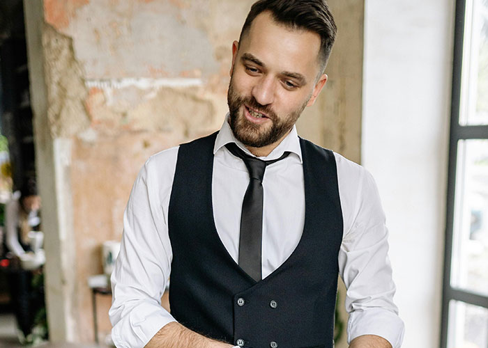 Camarero con uniforme negro sonriendo en restaurante, representando citas terribles contadas por camareros.