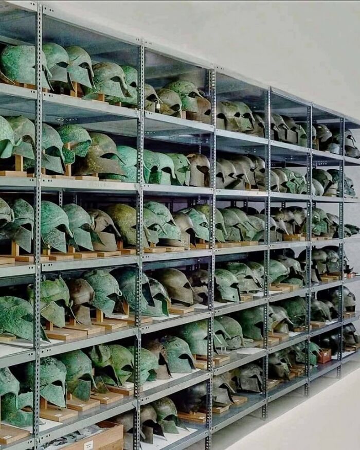Estanterías con cascos antiguos de bronce, parte de increíbles descubrimientos arqueológicos para estudio educativo.