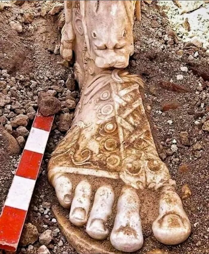 Escultura arqueológica antigua de un pie decorado con símbolos, excavada durante descubrimientos arqueológicos significativos.
