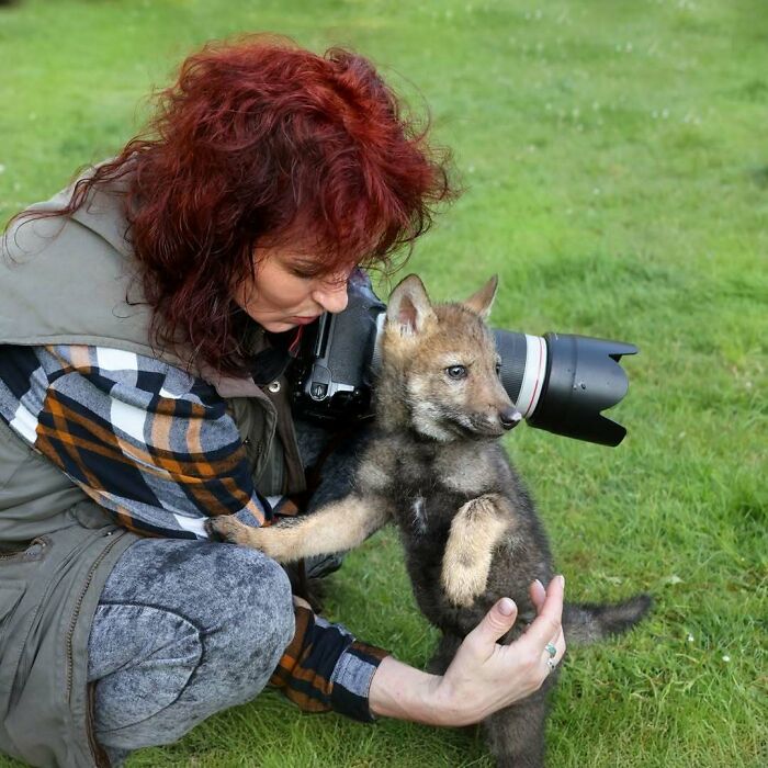 Fotógrafa de la naturaleza interactuando con un cachorro mientras intenta capturar imágenes en un entorno al aire libre.