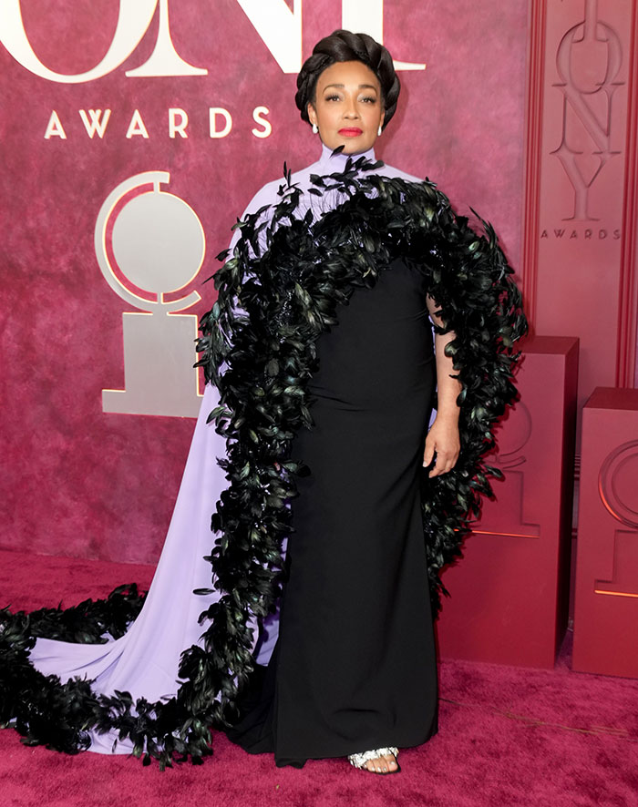 Mujer con vestido negro y capa de plumas negras en alfombra roja, ejemplo de malas decisiones de vestuario en Premios Tony.
