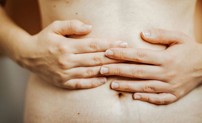 Manos sobre el abdomen de una persona, representando expertos en autopsias y hallazgos inquietantes sobre la muerte.