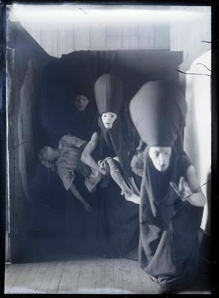 Personas con disfraces y máscaras inquietantes sosteniendo una figura en foto antigua inquietante del pasado.