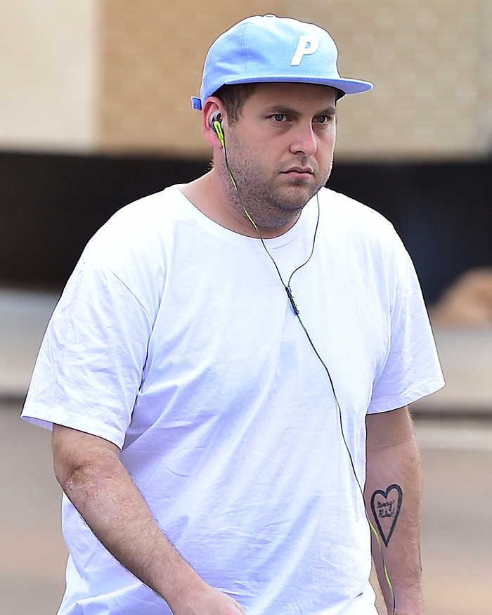 Hombre con tatuaje en el brazo y gorra azul, ejemplo de celebridades con peculiaridades corporales visibles al caminar.