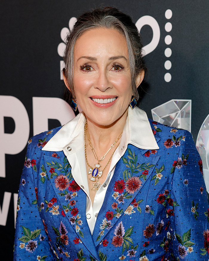 Mujer sonriente con peculiaridades corporales, vestida con traje azul floral en evento de celebridades.
