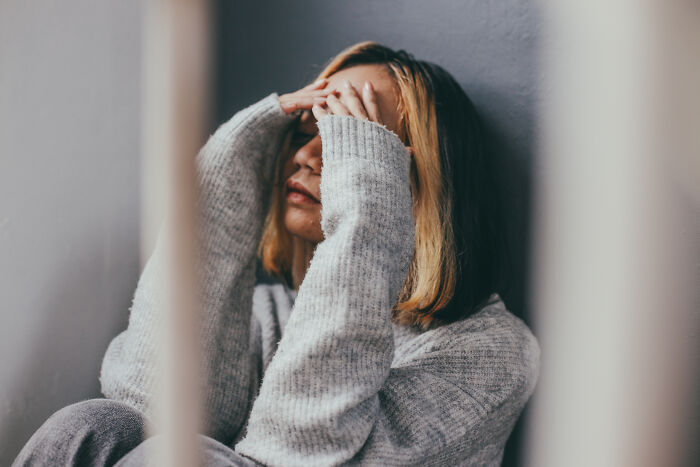 Mujer con suéter gris sentada y cubriéndose el rostro mostrando ansiedad y juicio en terapia psicológica.