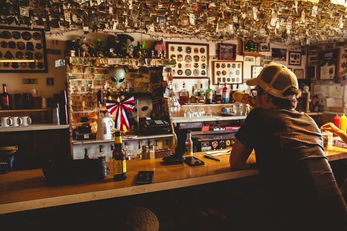 Hombre con gorra tomando una cerveza en un bar decorado con billetes y objetos curiosos, genes buenos o malos.