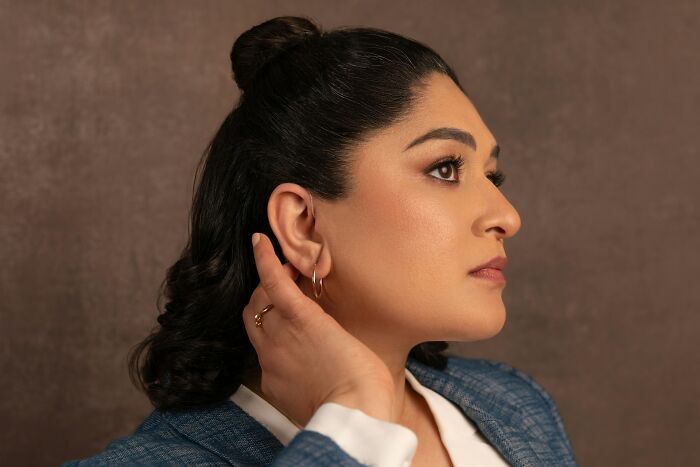 Mujer con genes únicos y rasgos marcados posando de perfil con expresión serena y fondo marrón liso.