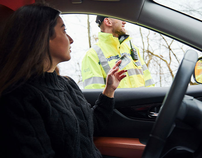 Mujer mostrando identificación a policía en control, ilustrando errores comunes de clientes según abogados expertos.