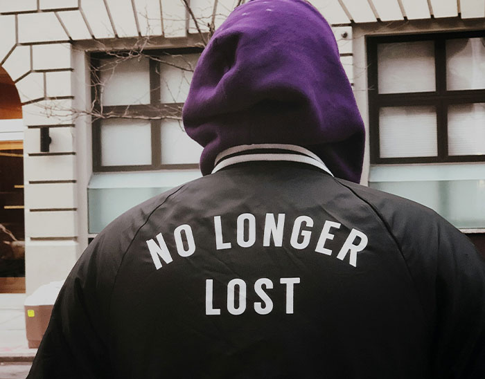 Persona con sudadera morada y chaqueta negra con texto no longer lost en la espalda, ilustrando estupideces de clientes abogados.