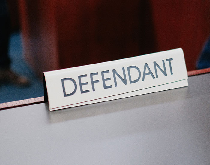 Cartel de escritorio con la palabra defendant en un juzgado representando casos y abogados con clientes en problemas legales.
