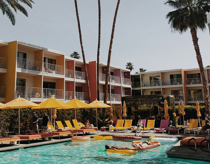 Piscina en hotel con gente descansando bajo sombrillas amarillas, ambiente relajado y cálido en zona turística palmada.